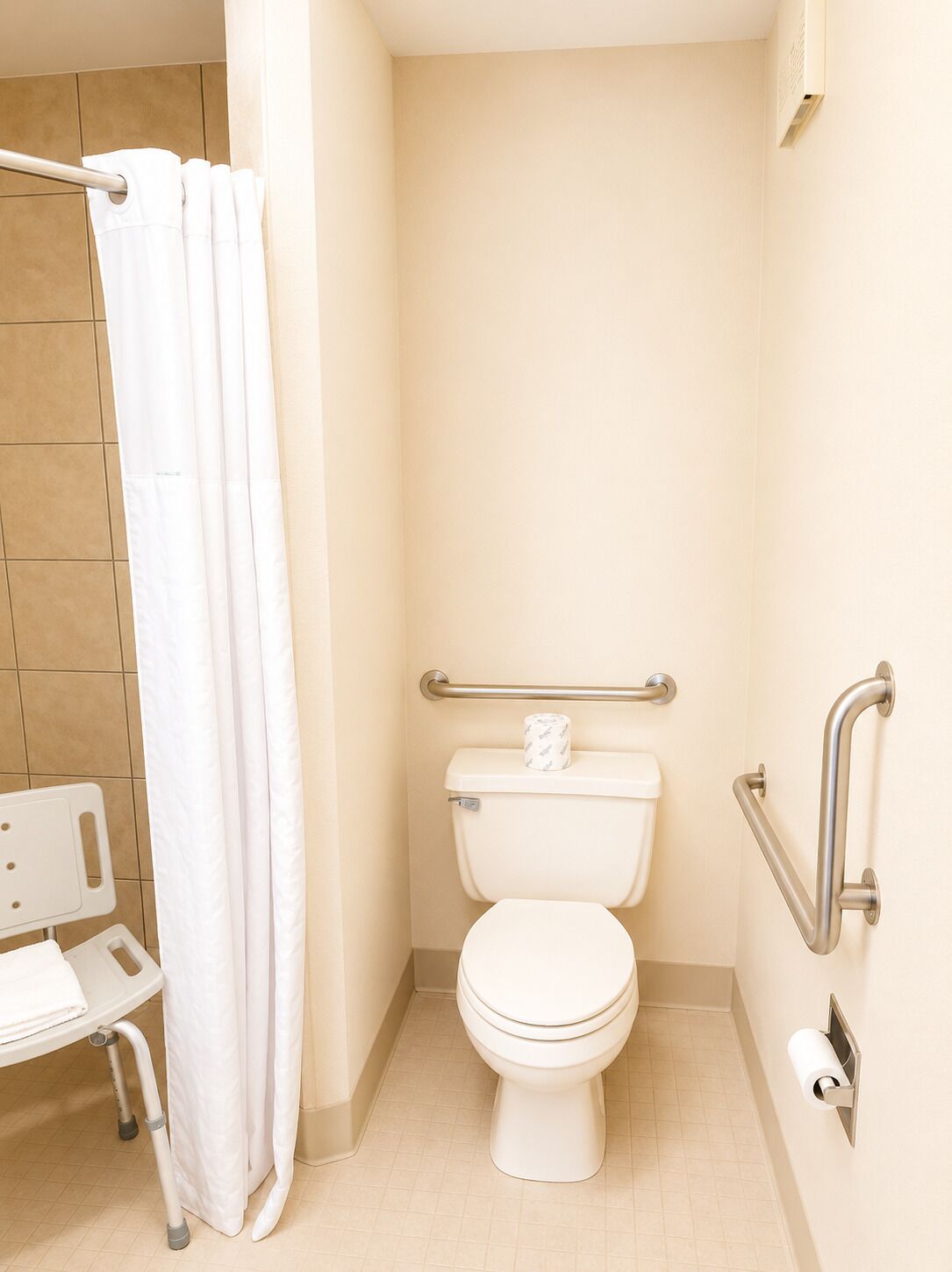 Une salle de bain équipée de toilettes, d’un rideau de douche, d’une barre d’appui et d’un banc accessible aux personnes en fauteuil roulant.
