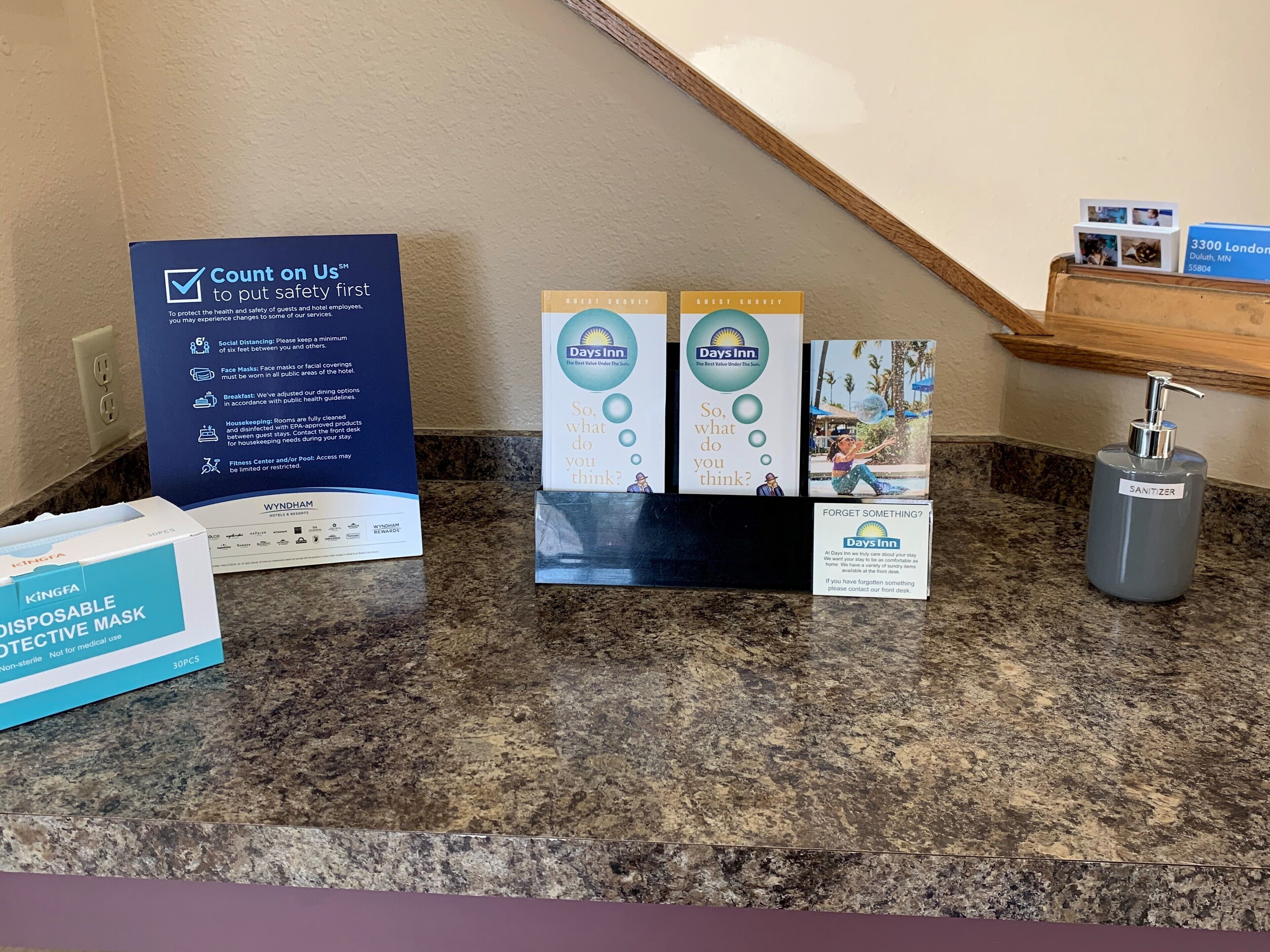 Zona de recepción de un hotel con un cartel que dice 'Count on Us', folletos de Days Inn, una caja de mascarillas desechables y un dispensador de desinfectante.