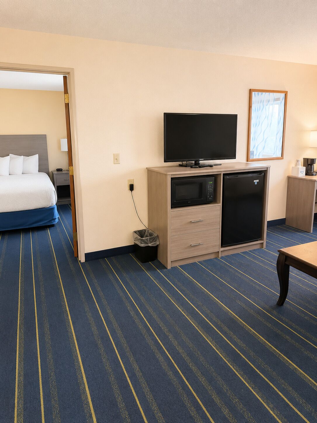 A hotel room with a bed, a television, a microwave, a refrigerator, a trash bin, and a table.