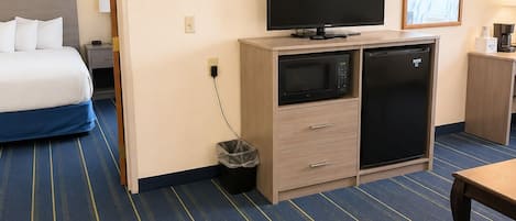 A hotel room with a bed, a television, a microwave, a refrigerator, a trash bin, and a table.
