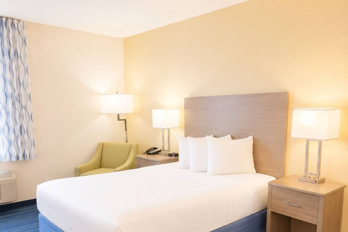 A hotel room with a large bed, two bedside tables with lamps, a chair, and a wall-mounted air conditioner.