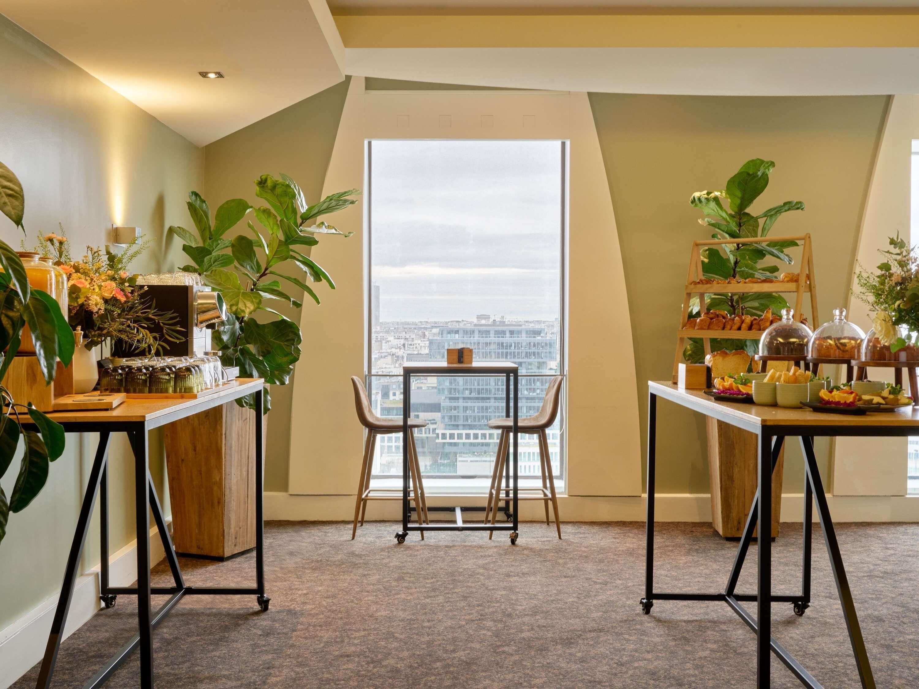 A modern room with a large window, two tables with plants, and a view of the cityscape.