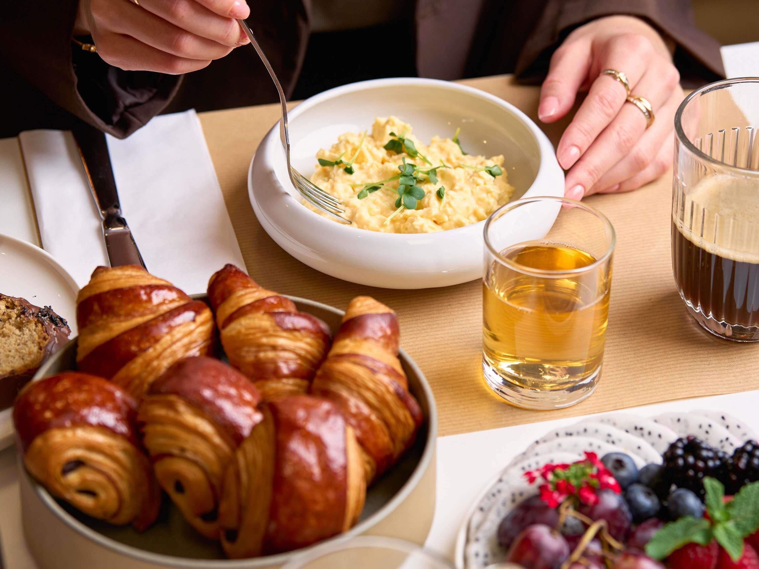 Ein Esstisch mit Croissants, Rührei und einem Glas Bier.