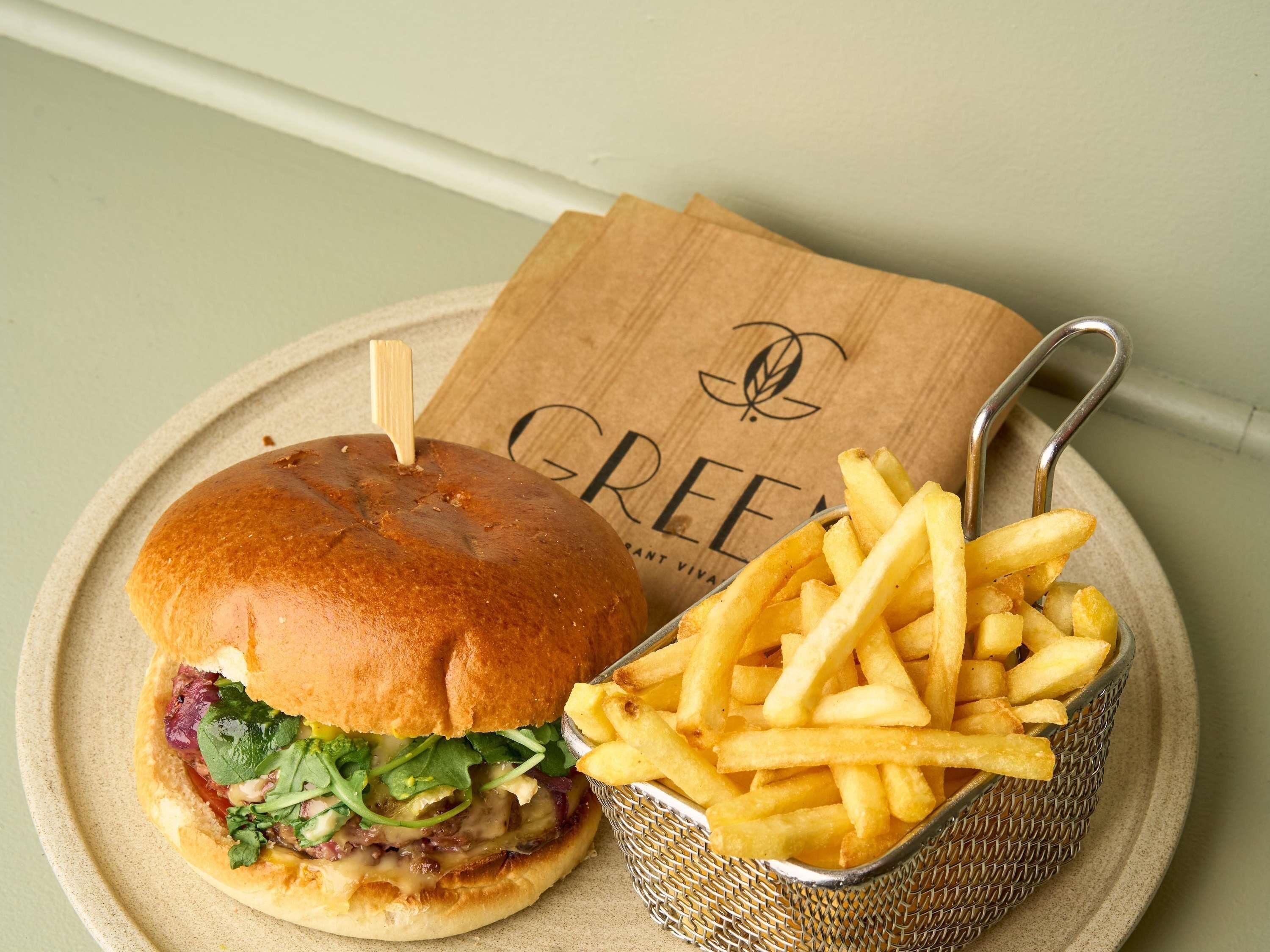 Un sándwich con papas fritas en un plato, una servilleta de madera con un logotipo y un tenedor de metal.