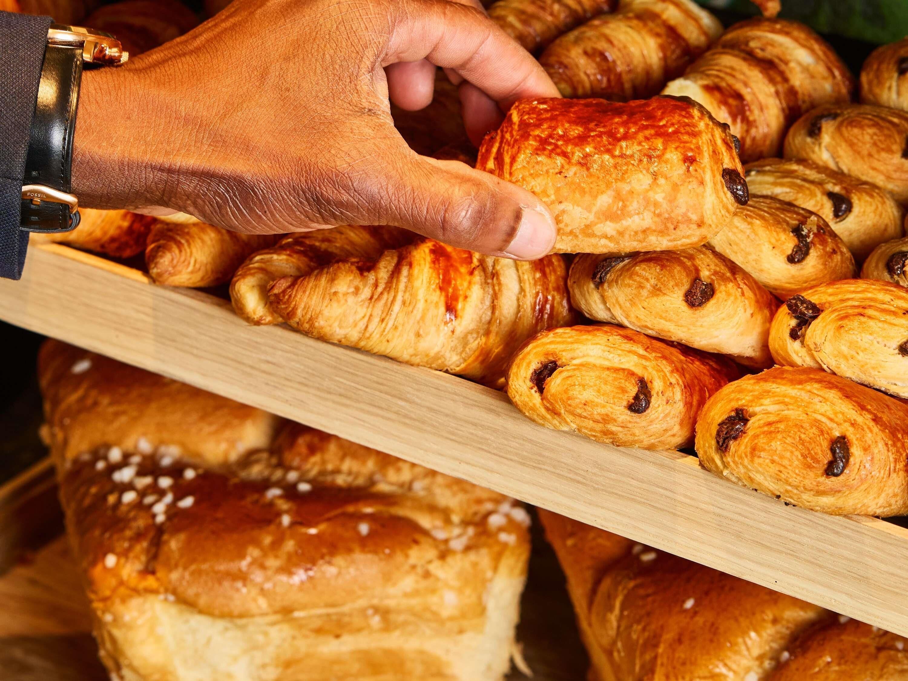 A hand selecting a pastry from a wooden display.