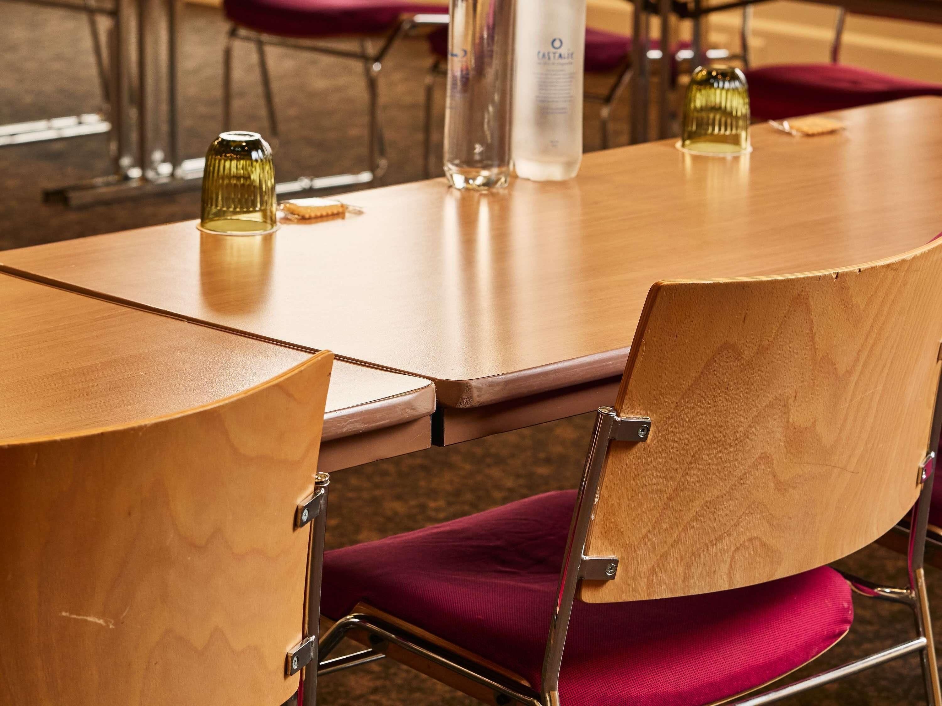 A wooden table with a chair that has a metal frame and a red cushion.