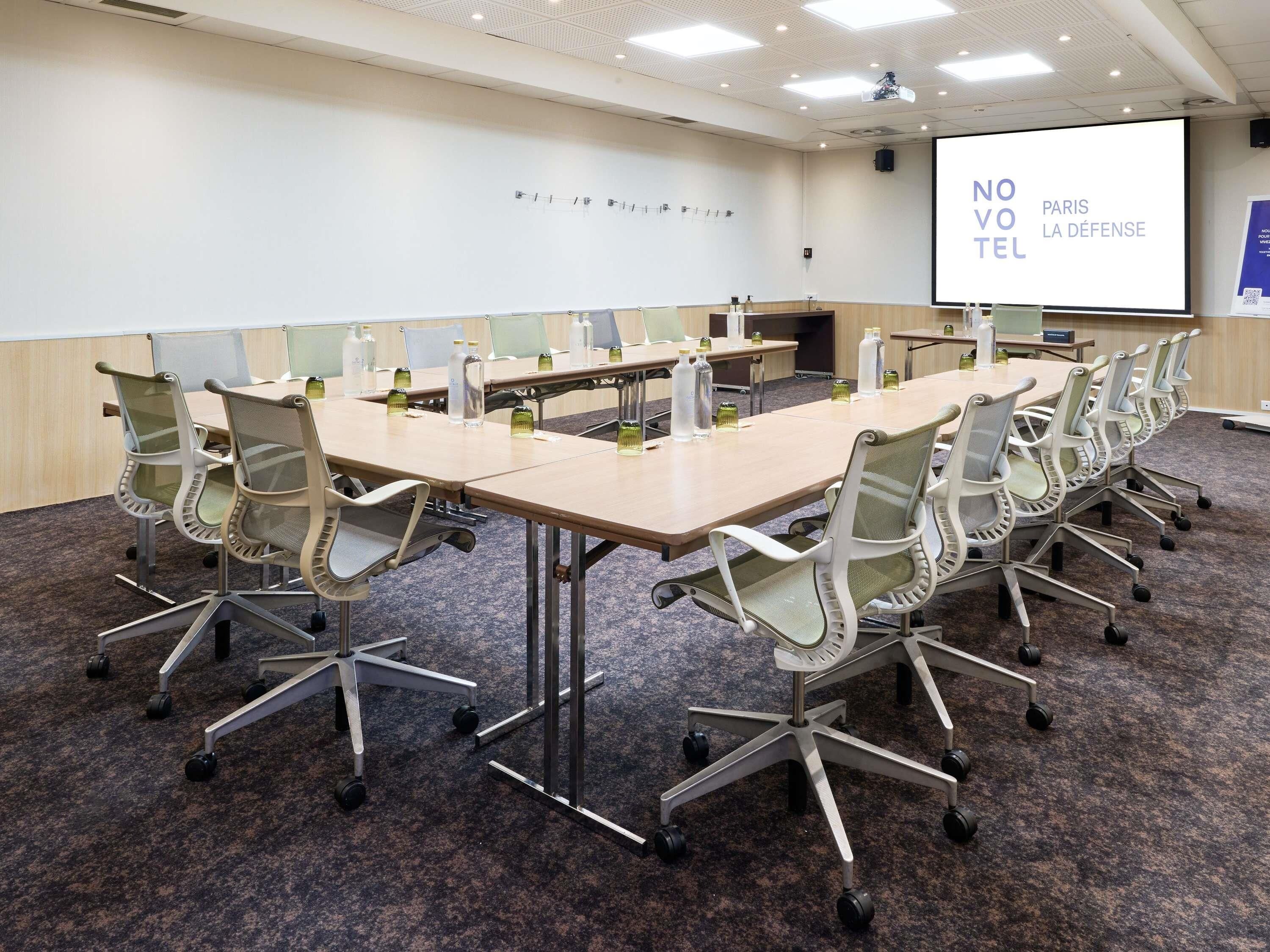 A conference room with a long table, chairs, a projector screen, and a presentation on defense.