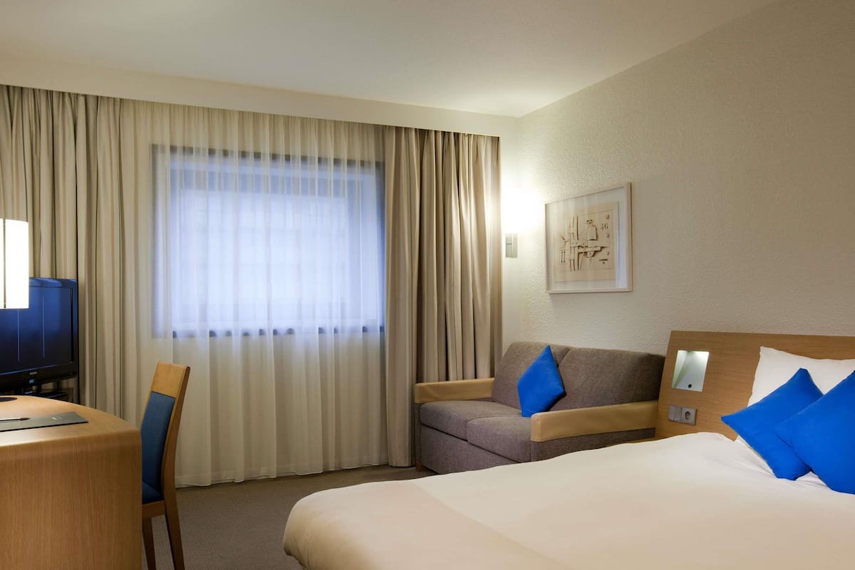 A hotel room with a bed, a desk, a chair, a sofa, and a television.