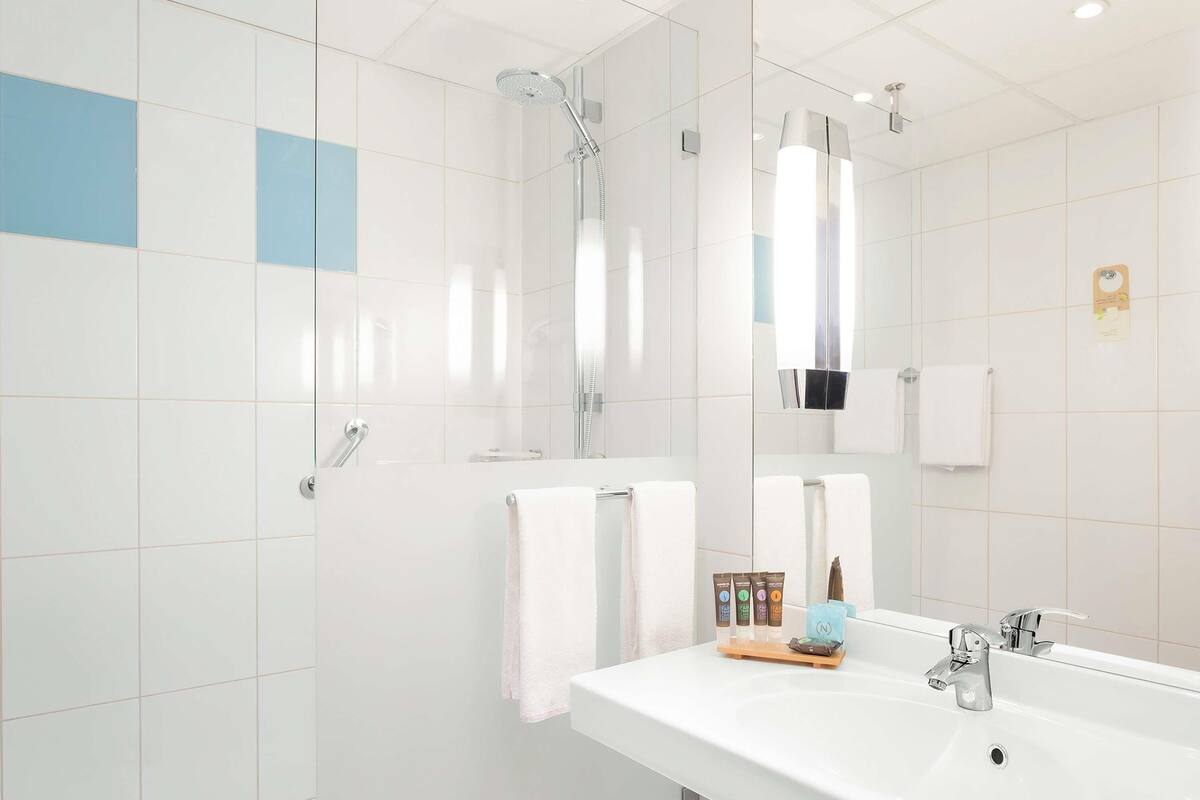 A modern bathroom with a large mirror, a shower, a sink, and a towel rack.