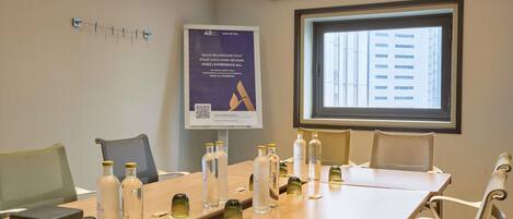 A meeting room with a long table, chairs, a projector screen, and a banner on the wall.
