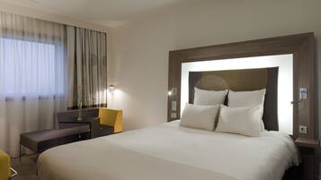 A hotel room with a large bed, a desk, a chair, and a window with curtains.