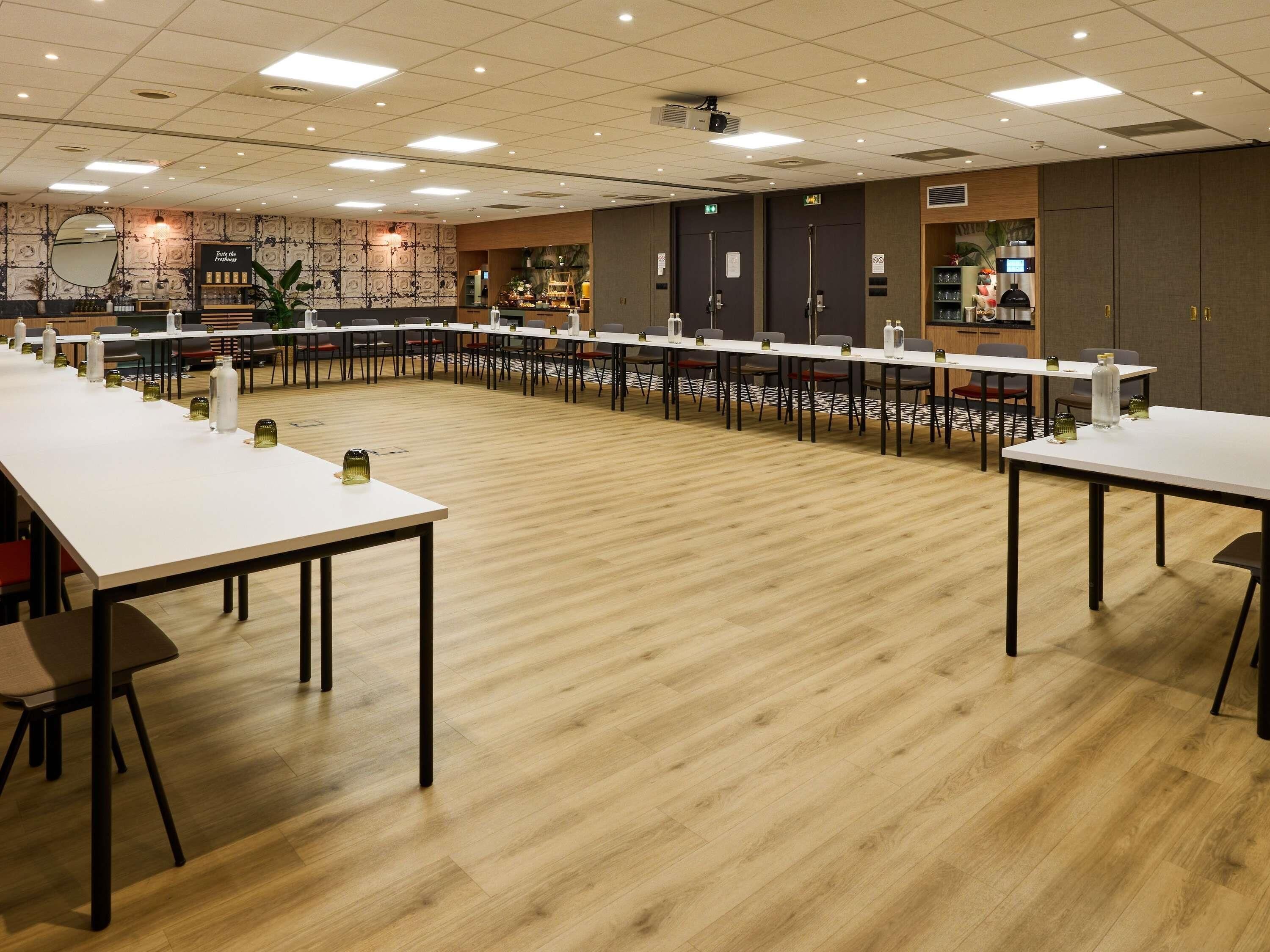 A conference room with long tables, chairs, and a projector screen.