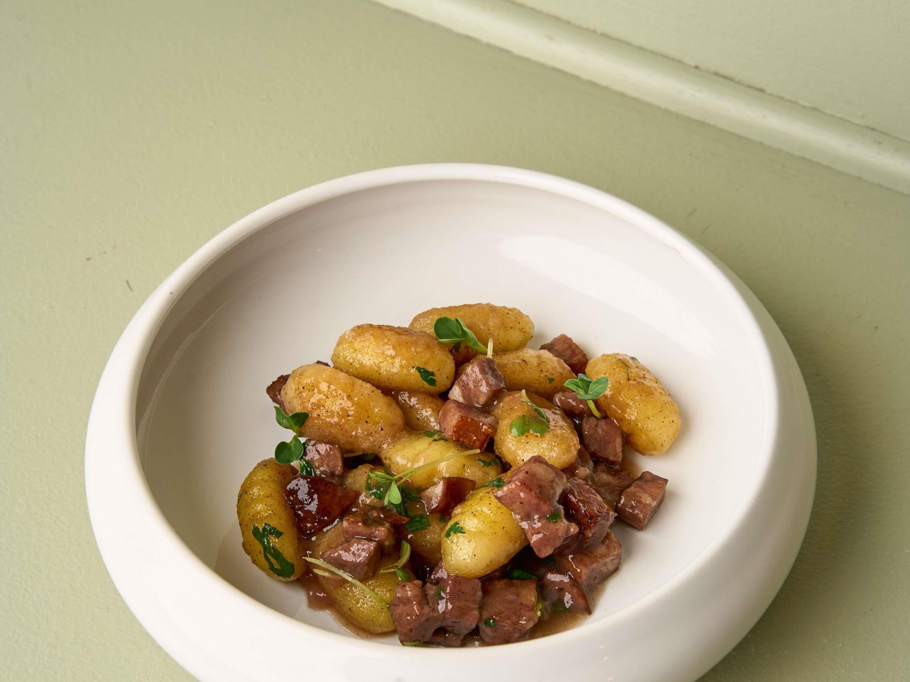 Een witte schaal met een gerecht gnocchi, vlees en kruiden.