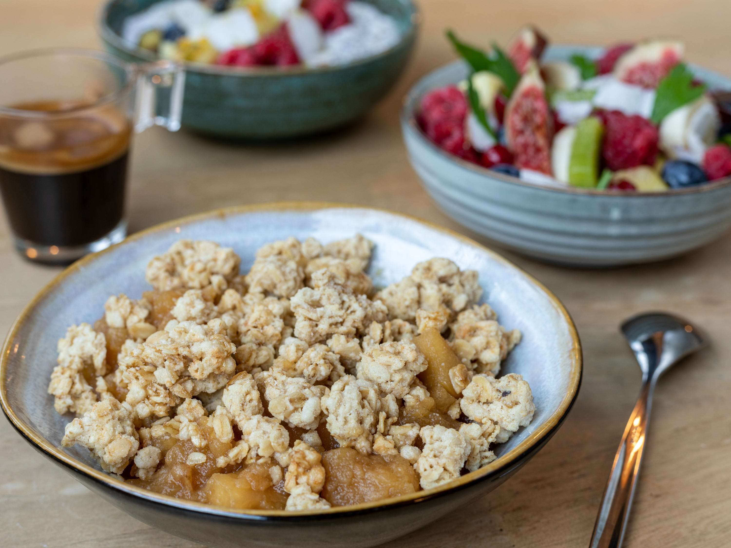 A bowl of granola with fruit, a glass of iced coffee, and a bowl of mixed berries and yogurt.