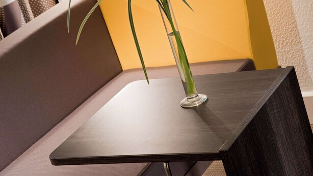 A modern, dark wooden table with a clear glass vase containing a green plant. - Novotel Paris La Défense Esplanade (Courbevoie)