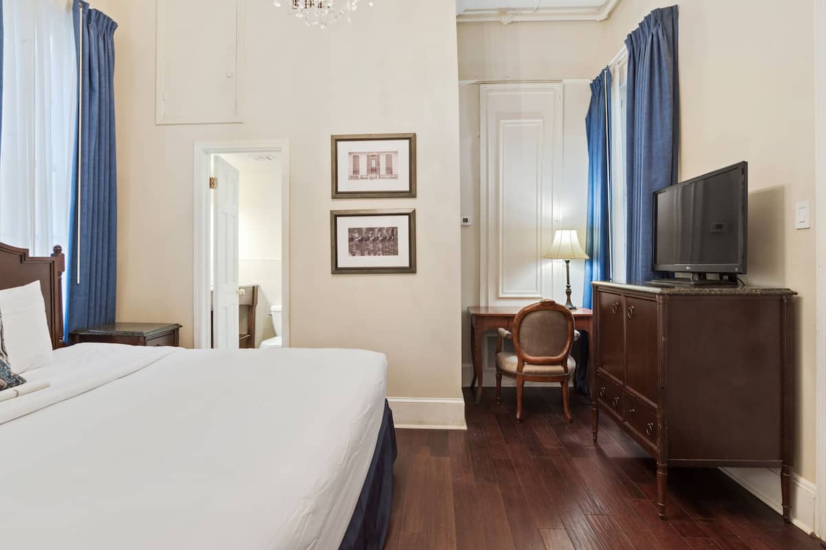 A hotel room with a large bed, a desk with a chair, a television on a cabinet, and two framed pictures on the wall.