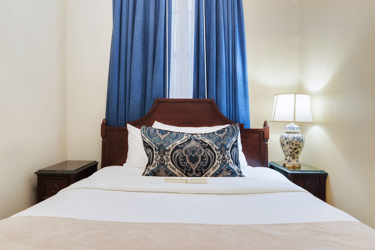 A neatly made bed with a patterned pillow, a wooden headboard, and a nightstand with a lamp and a vase.