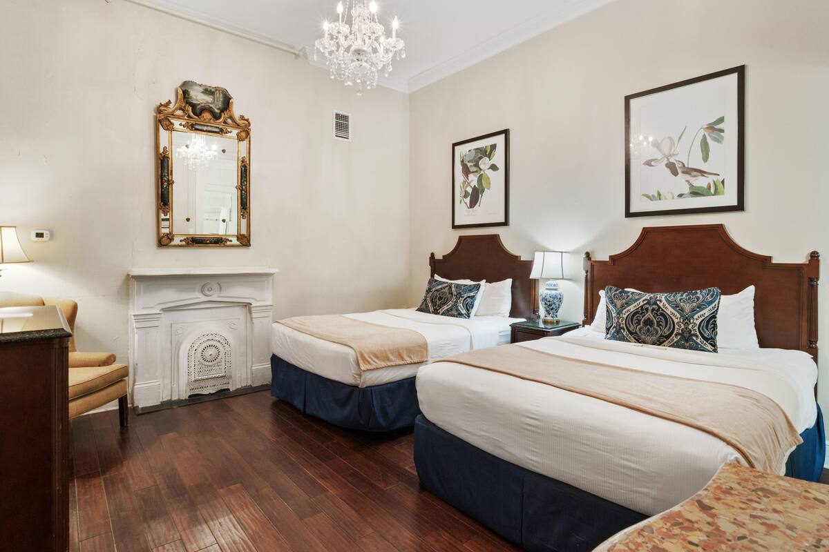 A hotel room with two beds, a chandelier, a fireplace, and framed artwork on the walls.