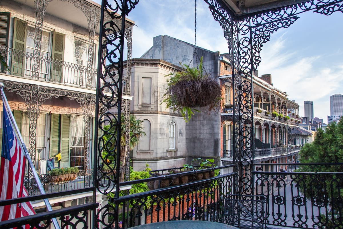 A balcony with wrought iron railings, a hanging plant, and a view of a cityscape with buildings and a flag.