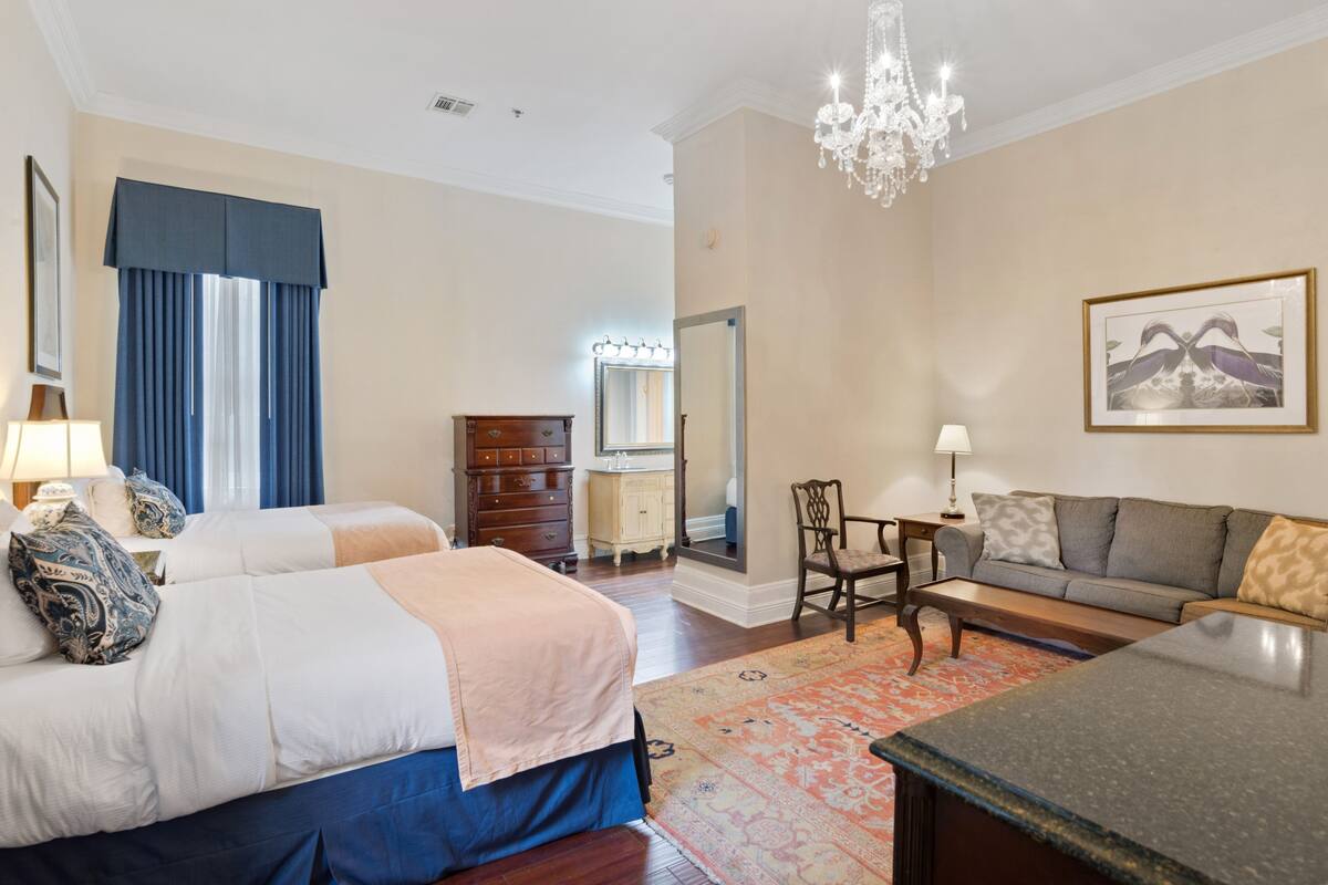 A hotel room with two beds, a sofa, a coffee table, a chandelier, and a mirror.