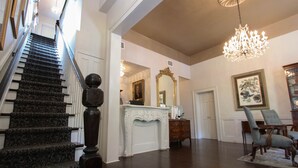 Un magnifique escalier recouvert d’une moquette à motifs sombres, une console blanche richement décorée, un grand miroir et un lustre.