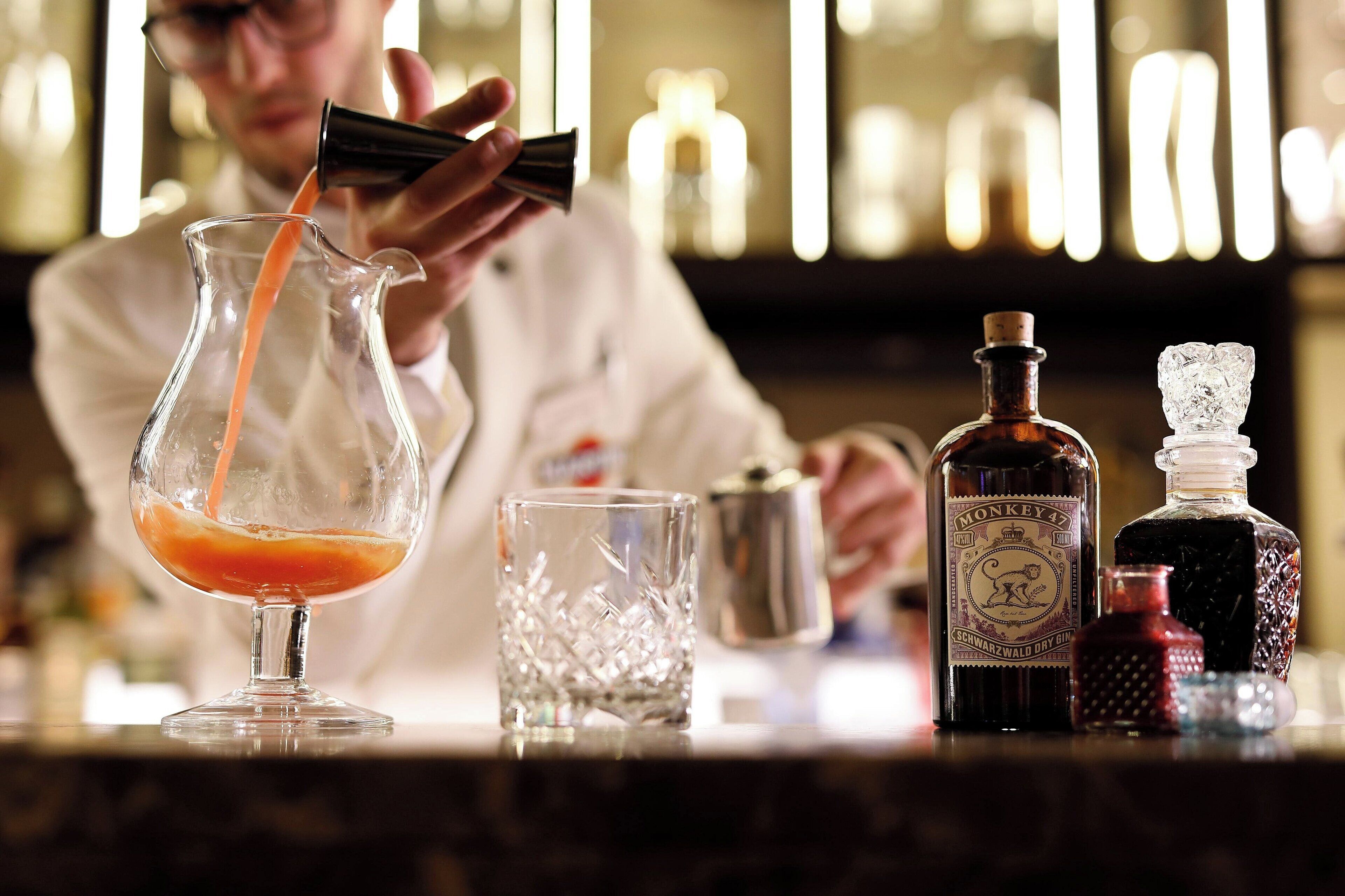A bartender pouring a drink into a glass pitcher.