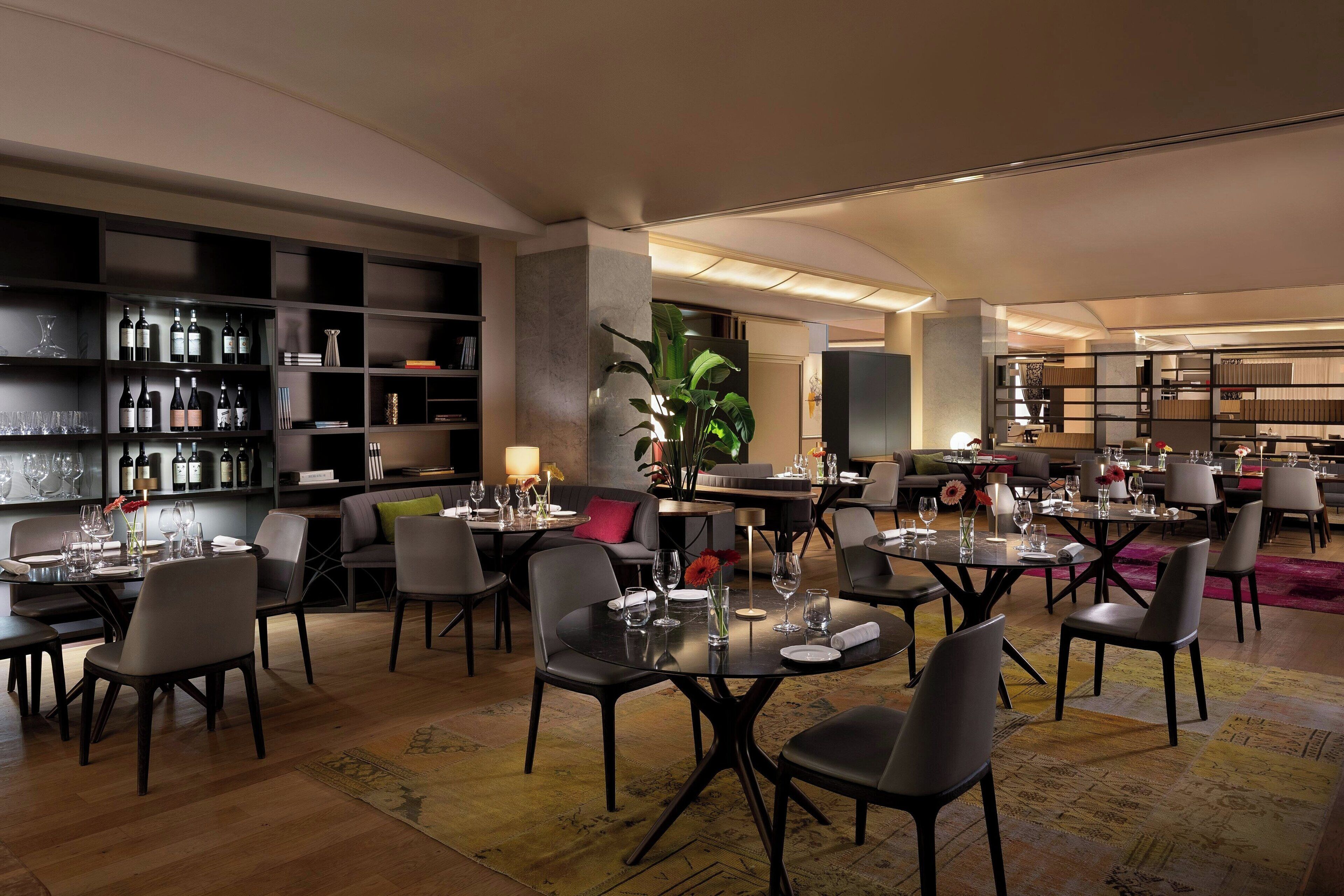 A modern dining area with tables set for guests, a wine display, and a cozy seating area.