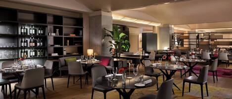 A modern dining area with tables set for guests, a wine display, and a cozy seating area.