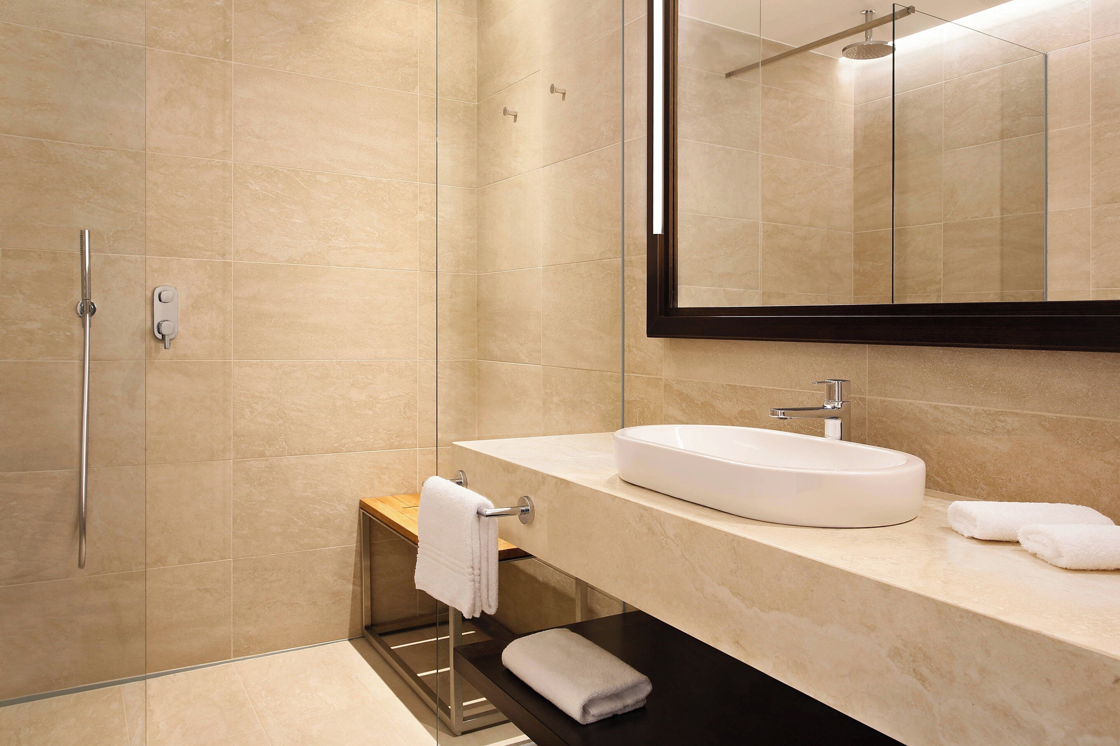 Une salle de bain moderne avec une douche à l’italienne en verre, un lavabo blanc et un grand miroir.