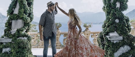 A couple dancing in an outdoor setting with a view of a body of water and mountains in the background.