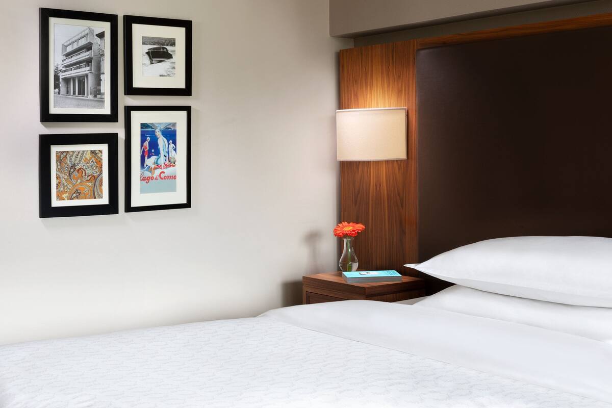 A hotel room with a bed, a nightstand with a lamp, and four framed pictures on the wall.
