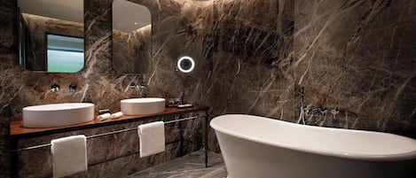 Un baño moderno con dos lavamanos, una bañera independiente y paredes de mármol.