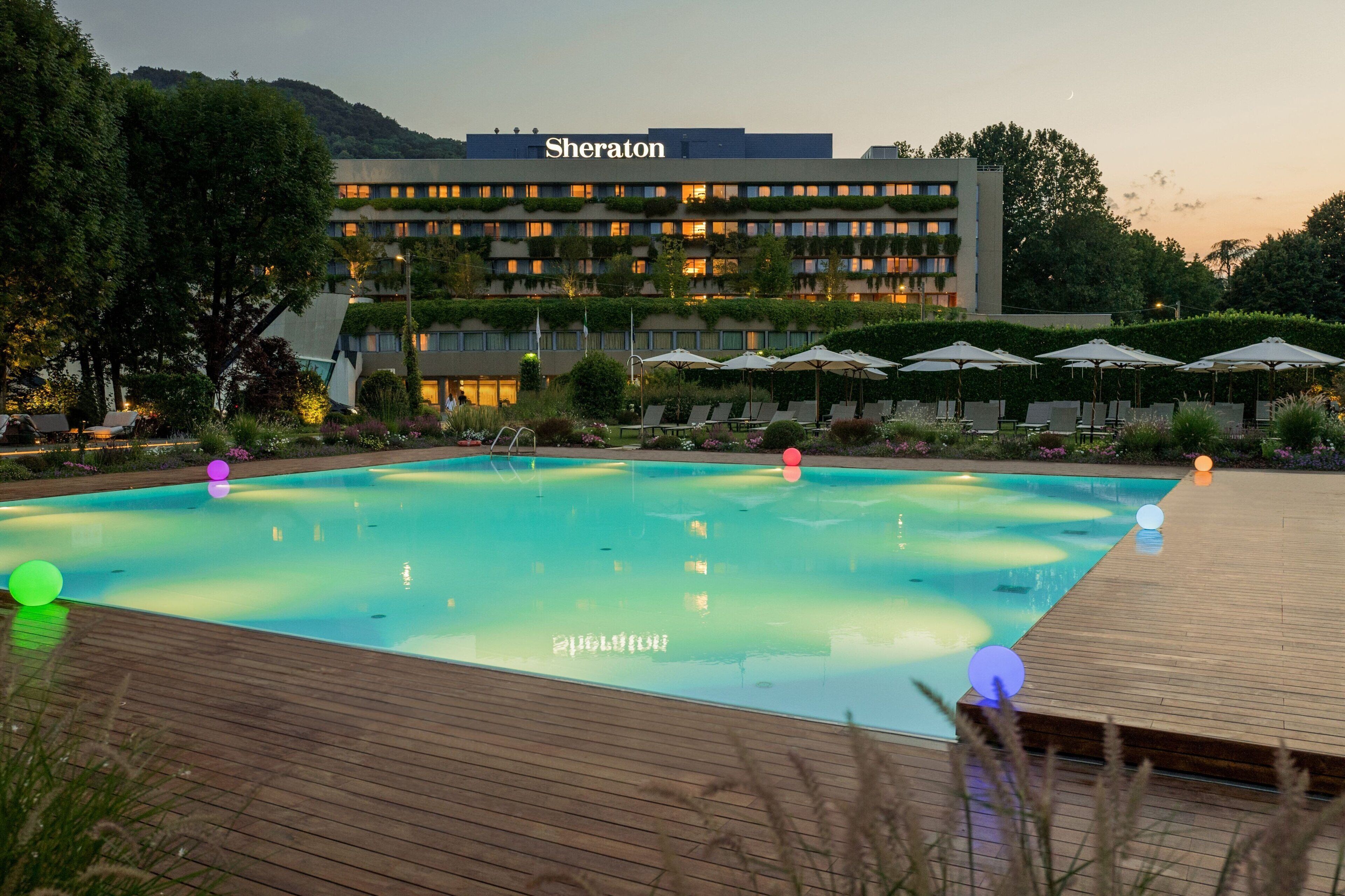 Un hotel chiamato 'Sheraton' con piscina, sedie a sdraio e ombrelloni.