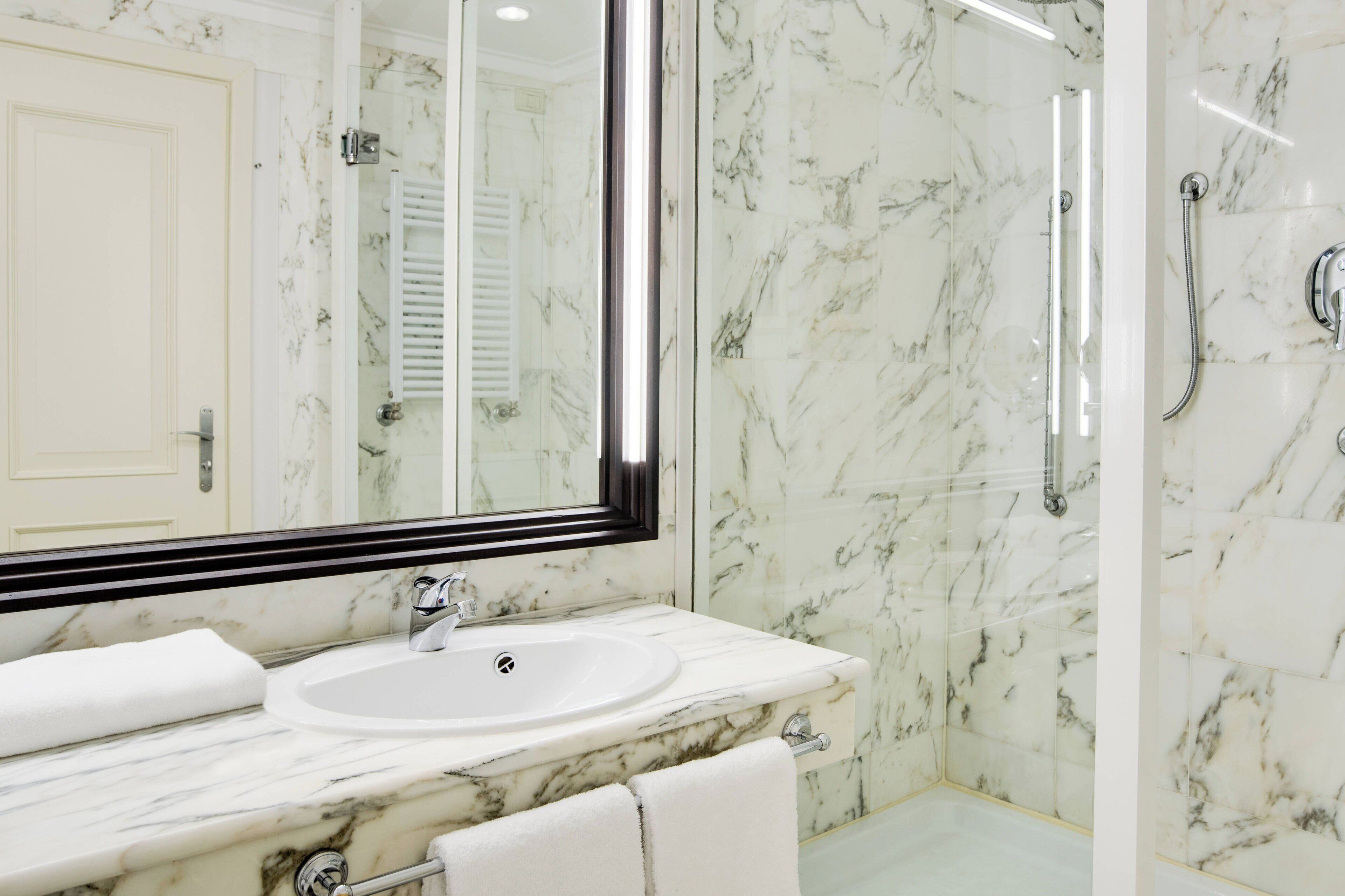 A bathroom with a marble sink, a large mirror, and a glass-enclosed shower.