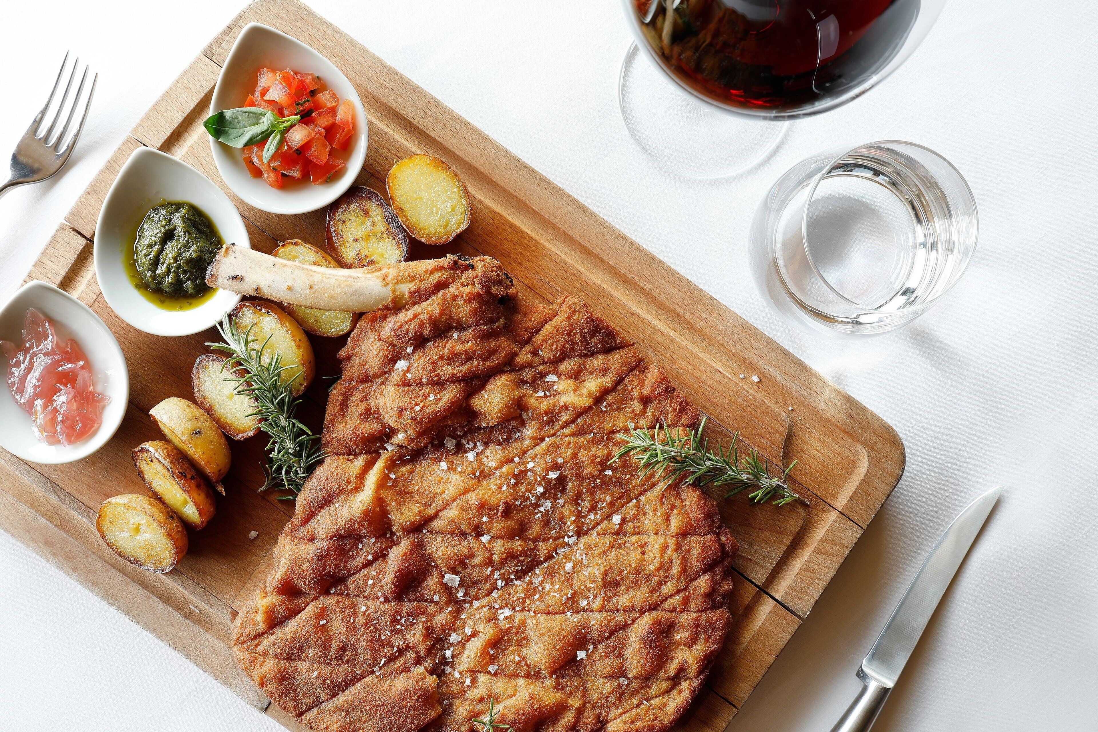A wooden cutting board with a grilled steak, roasted potatoes, and various sauces.