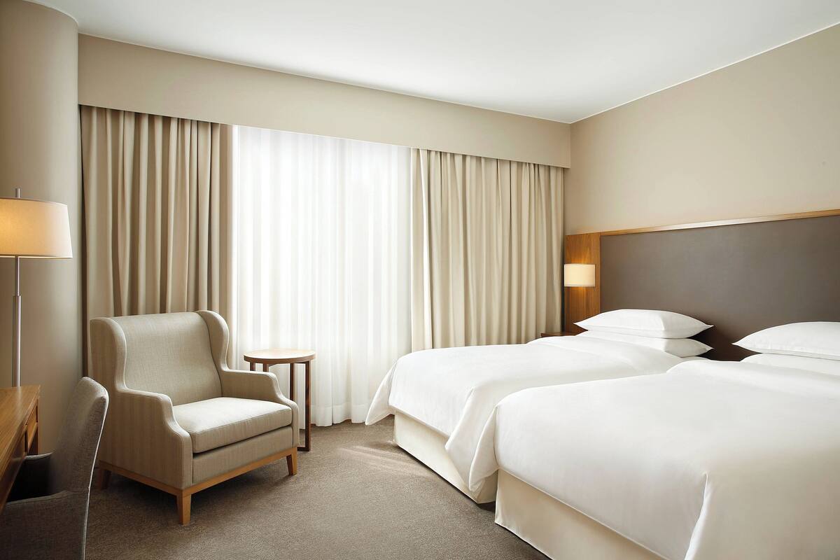 A hotel room with a sofa, two beds, a small table, and a lamp.