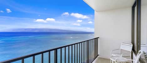 Un balcon avec vue sur l’océan, des chaises blanches et une porte vitrée.