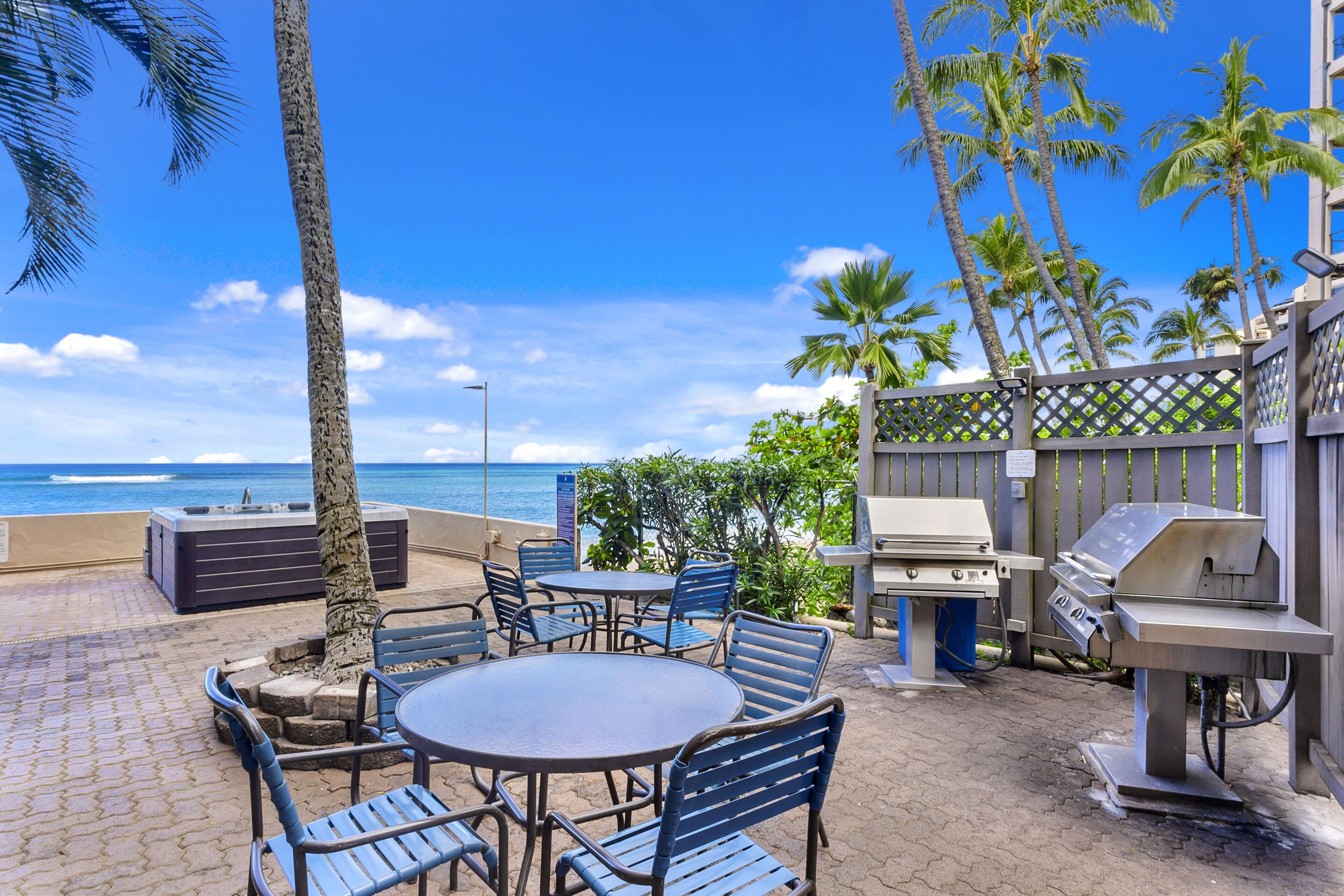 Une terrasse extérieure avec une table ronde et des chaises, un barbecue et une vue sur l’océan.