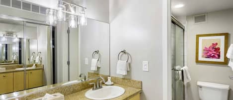A bathroom with a granite countertop, a white sink, a large mirror, a glass shower enclosure, and a toilet.