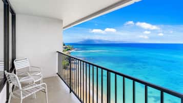 A balcony with a white metal chair, a view of the ocean, and a clear sky.