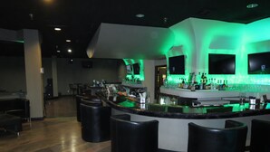 A bar area with a curved counter, black stools, and green ambient lighting. - Wyndham Garden Midland (Midland)