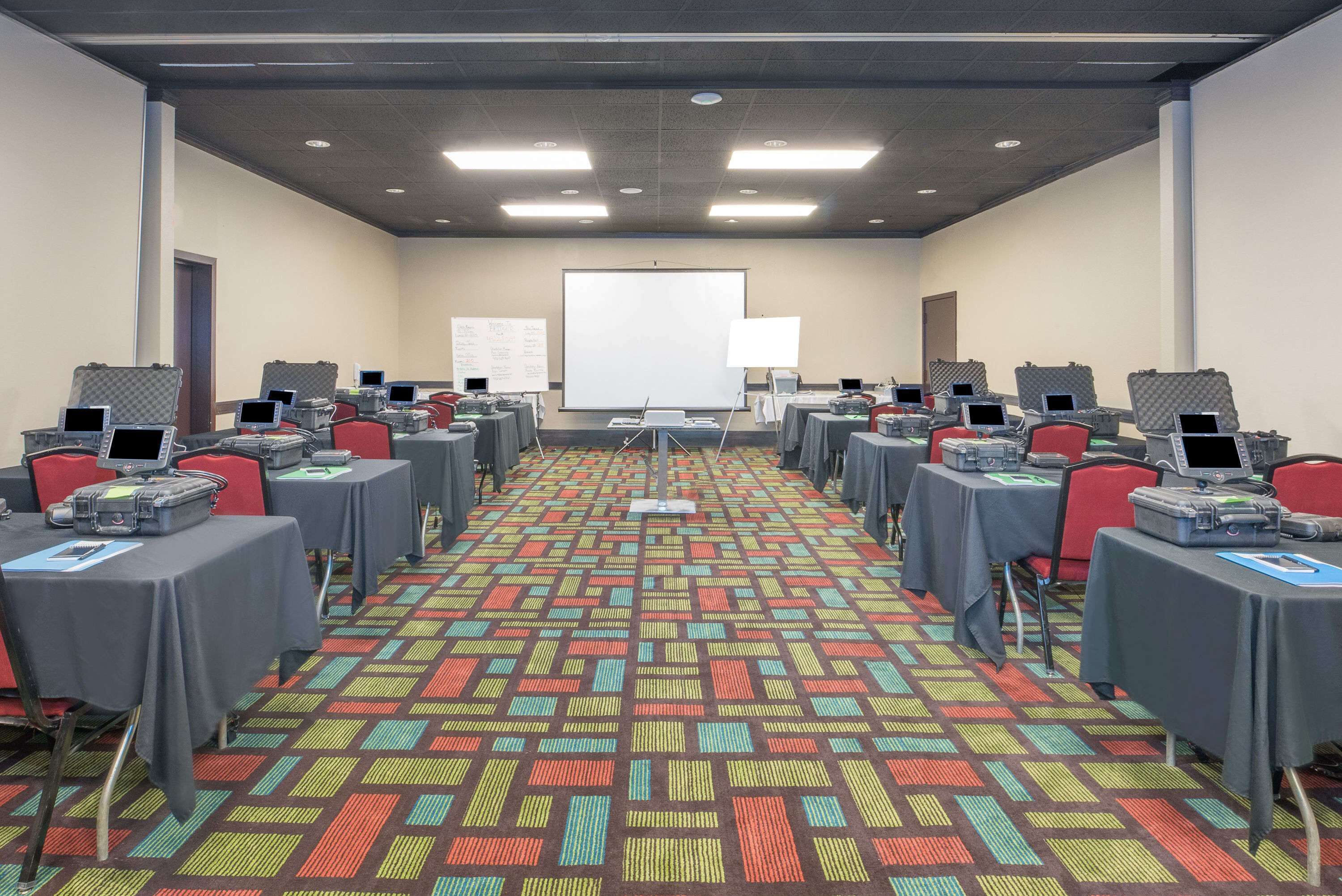 A conference room with multiple tables, each equipped with laptops and presentation screens, arranged in rows.