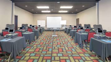 A conference room with multiple tables, each equipped with laptops and presentation screens, arranged in rows.