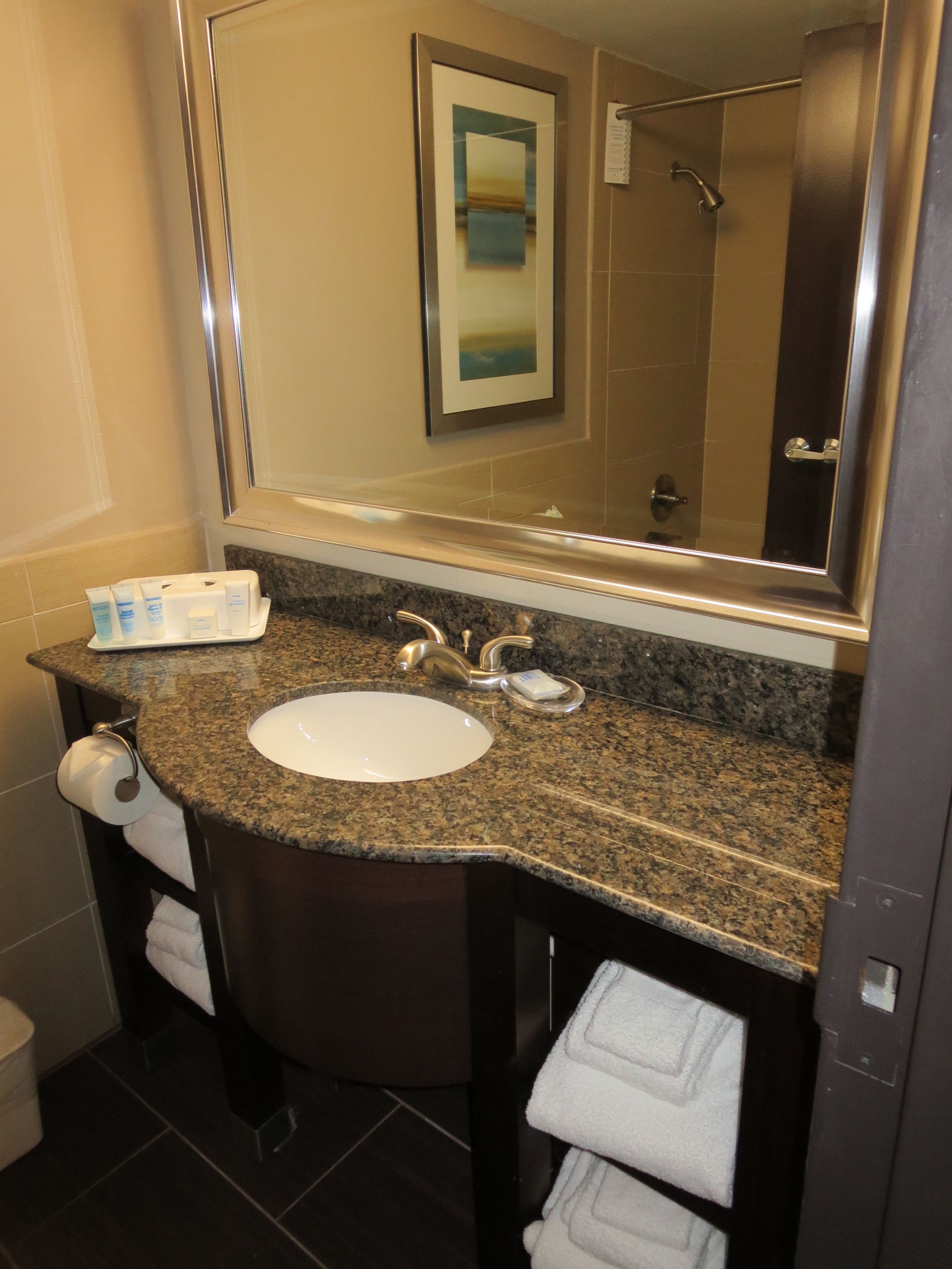A bathroom with a granite countertop sink, a mirror, and a towel rack.