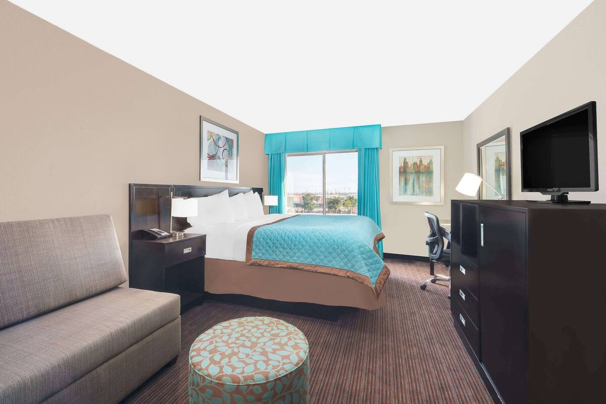 A hotel room with a bed, a sofa, a desk, a television, and a window with curtains.