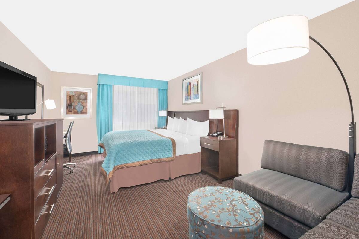 A hotel room with a bed, a desk, a television, a sofa, and a patterned ottoman.
