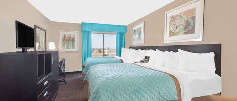 A hotel room with two beds, a TV, a desk, and a window with a city view.
