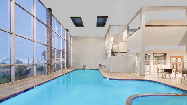 An indoor swimming pool with large windows, a wooden deck, and a seating area with tables and chairs. - Wyndham Garden Midland (Midland)