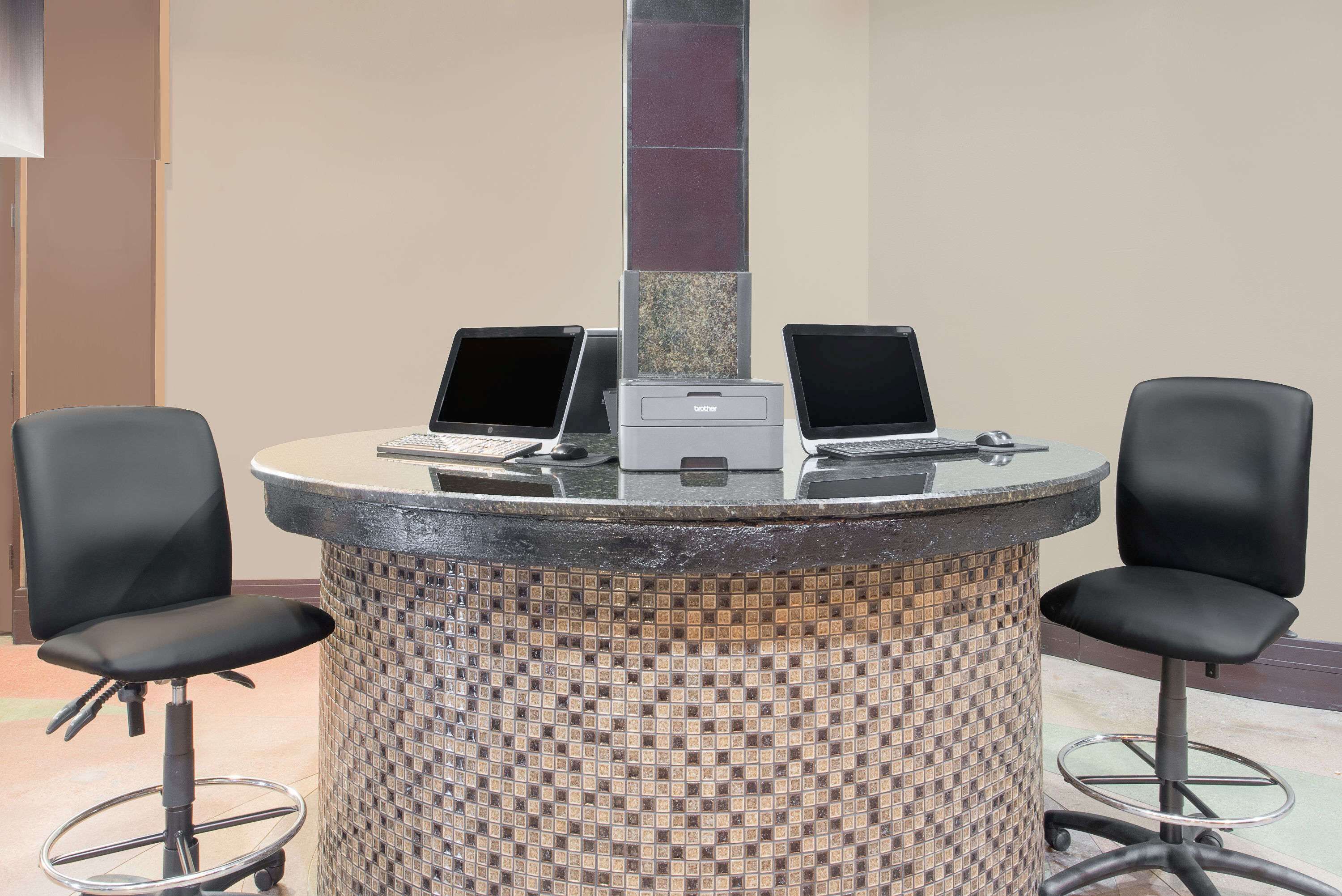 Ein runder Tisch mit zwei Laptops und einem Drucker, umgeben von zwei schwarzen Stühlen.