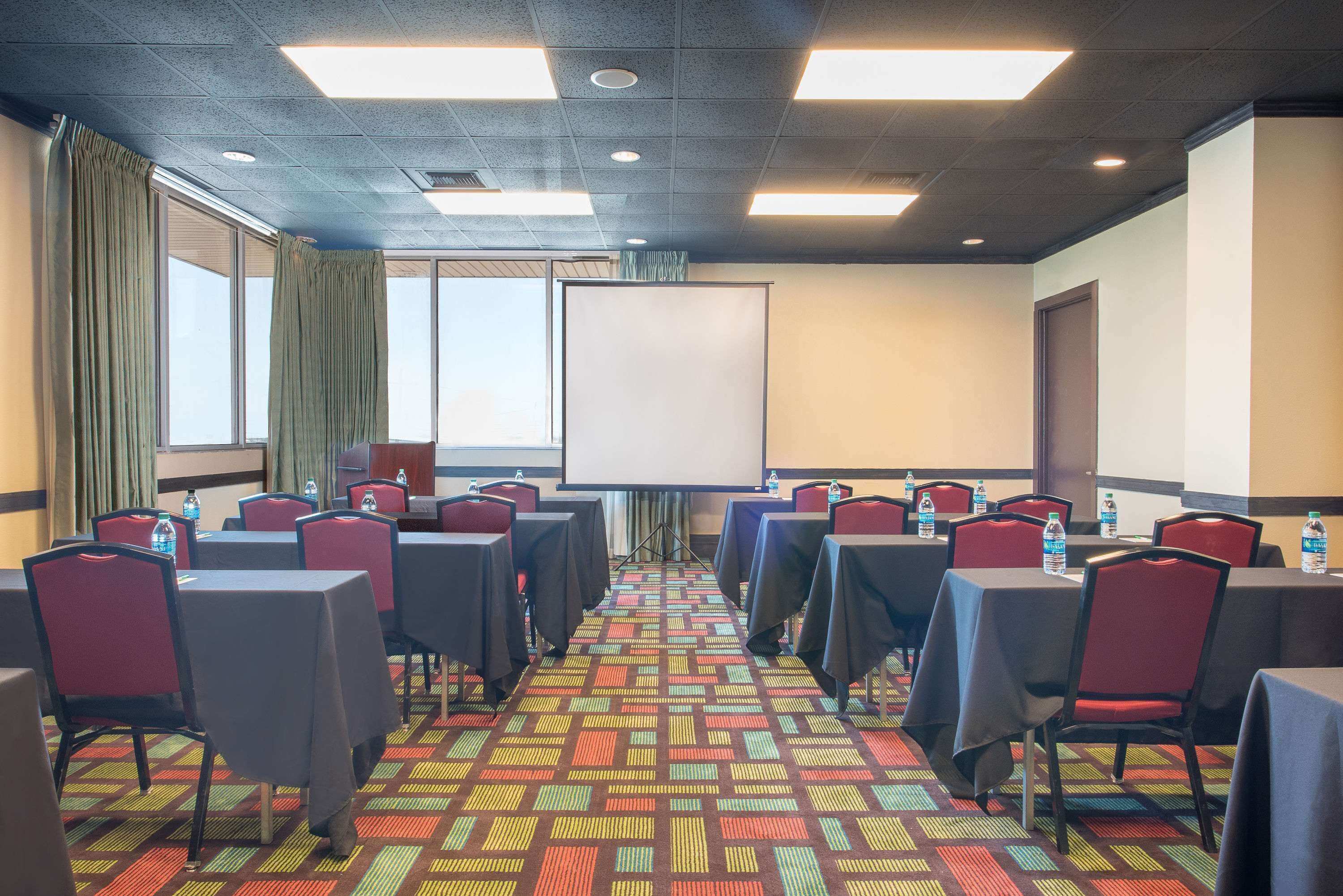 A conference room with tables and chairs, a projector screen, and a carpeted floor.